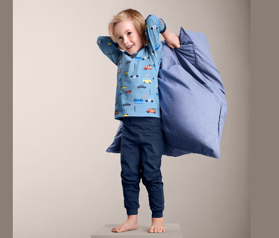 Junge steht auf einem Würfel und hält einen blauen Pyjama.