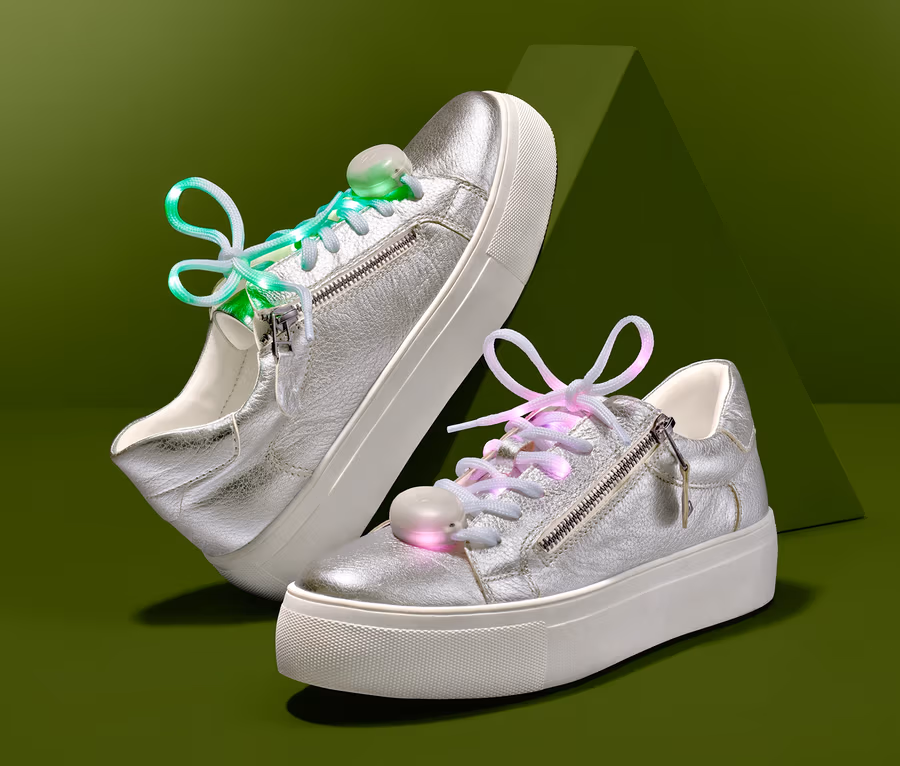Zwei silberne Schuhe mit LED-Leucht-Schnürsenkeln auf grünem Hintergrund.