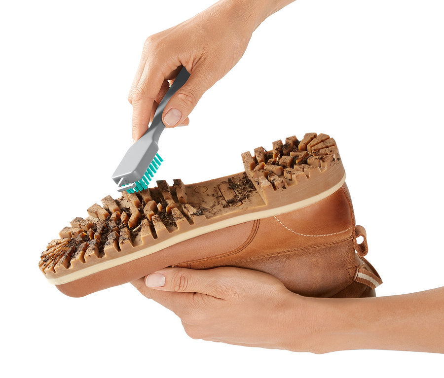 Eine Hand reinigt mit einem Grobschmutz-Schuhsohlenreiniger die Sohle eines braunen Lederschuhs.