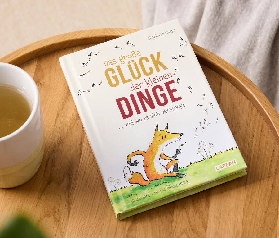 Buch "Das große Glück der kleinen Dinge" und eine Tasse Getränk auf einem Holztablett.