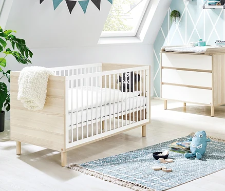 Ein Kinderzimmer mit Pinolino Babybett »Flow«, Kommode und blauem Teppich.