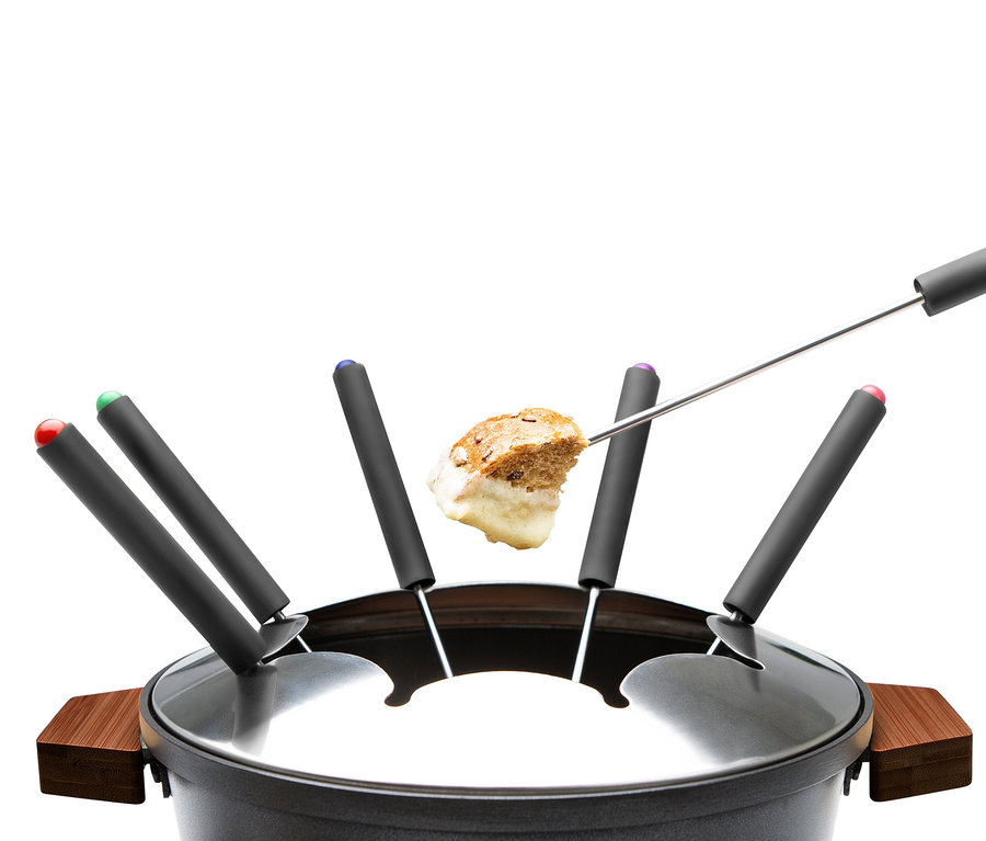 Ein Stück Brot, das in Fondue getunkt ist, wird über einem schwarzen Topf mit farblich gekennzeichneten Gabeln gehalten.