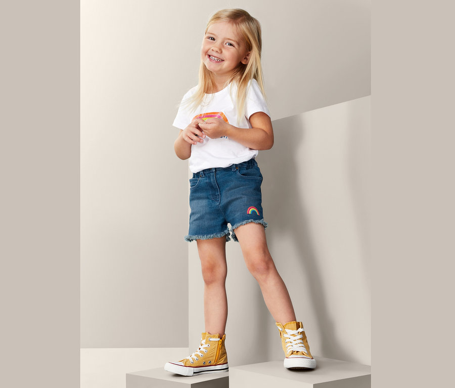 Lächelndes Mädchen trägt Denim-Shorts und T-Shirt.