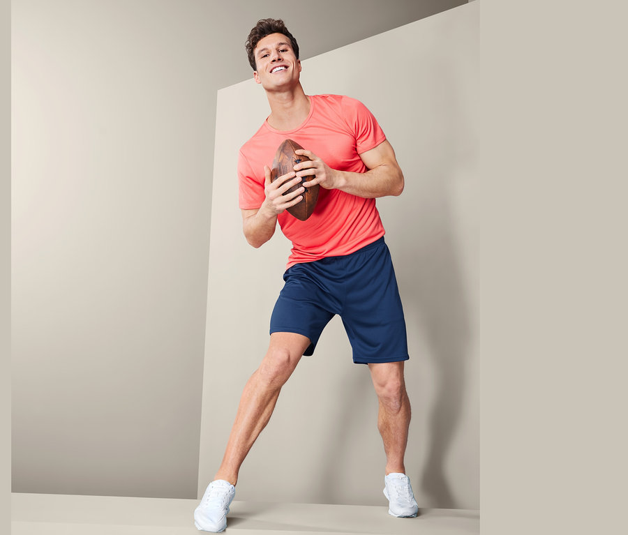 Mann hält Football und trägt Sportshorts.