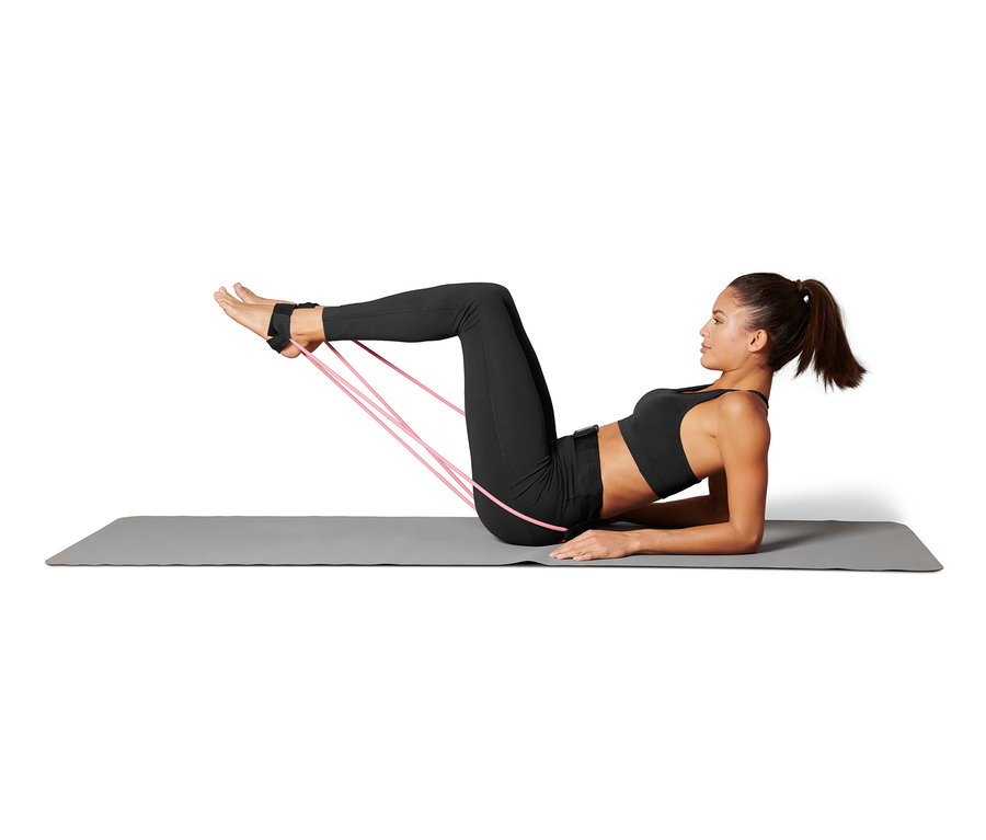 Frau liegt auf einer Matte und trainiert mit einer Fitnesstube, die an ihren Füßen befestigt ist.
