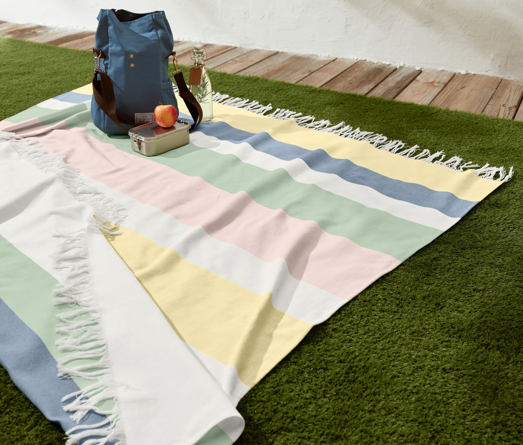 Gestreiftes XL-Picknicktuch mit Fransen auf Gras mit Tasche, Lunchbox, Apfel und Wasserflasche.