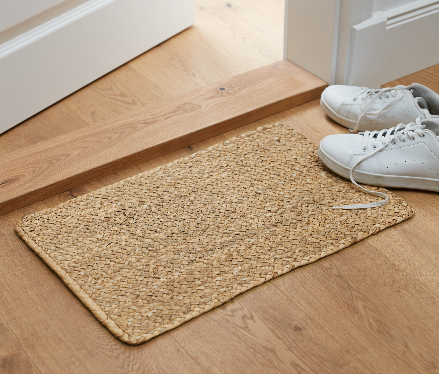 Vor einer offenen Tür liegt ein Teppich aus Wasserhyazinthe, daneben stehen Schuhe.