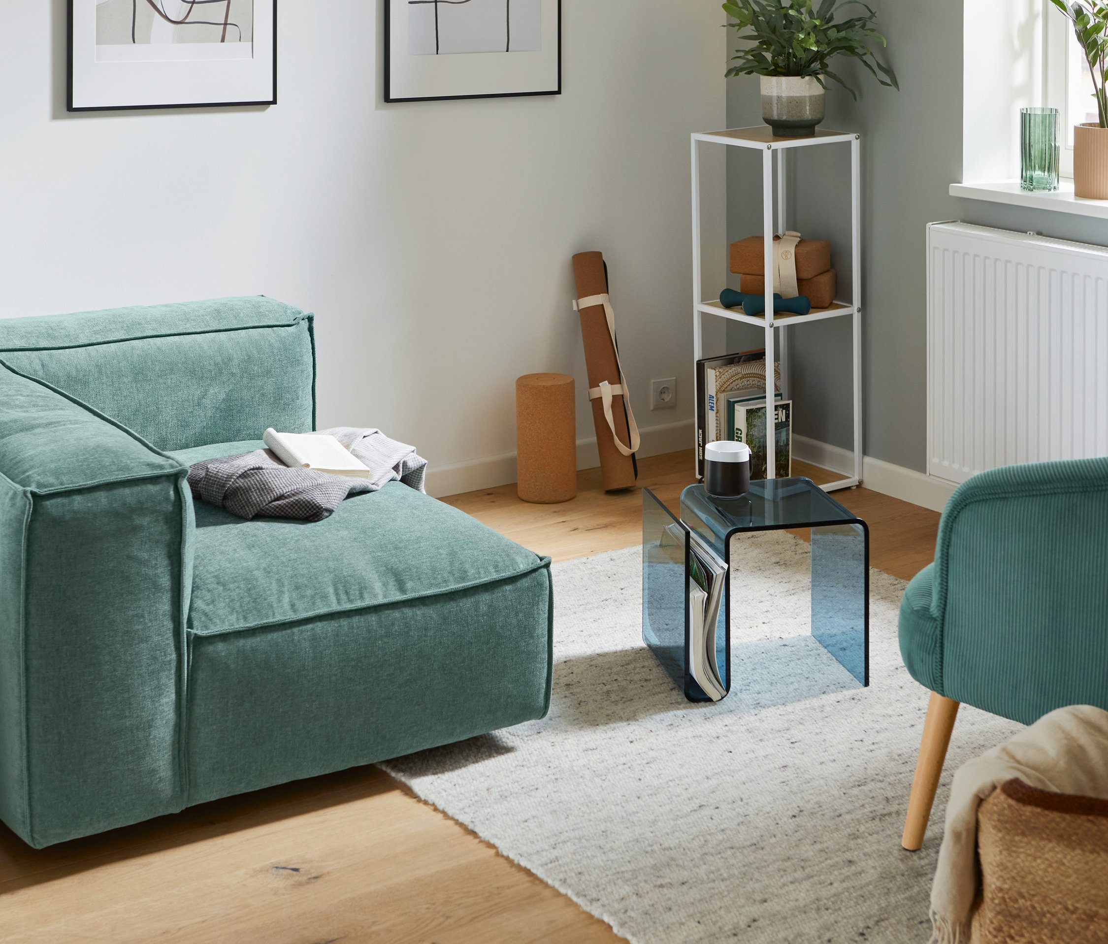 Ein Eckelement rechts des SCAPA Modul-Sofas »Berlin« steht neben einem kleinen Standregal und einem Beistelltisch aus Acrylglas.