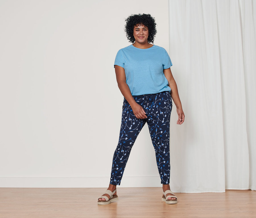 Frau steht und trägt ein hellblaues Shirt aus Leinenmix, eine dunkelblaue Jerseyhose mit Alloverprint und Plateau-Sandale aus Leder.