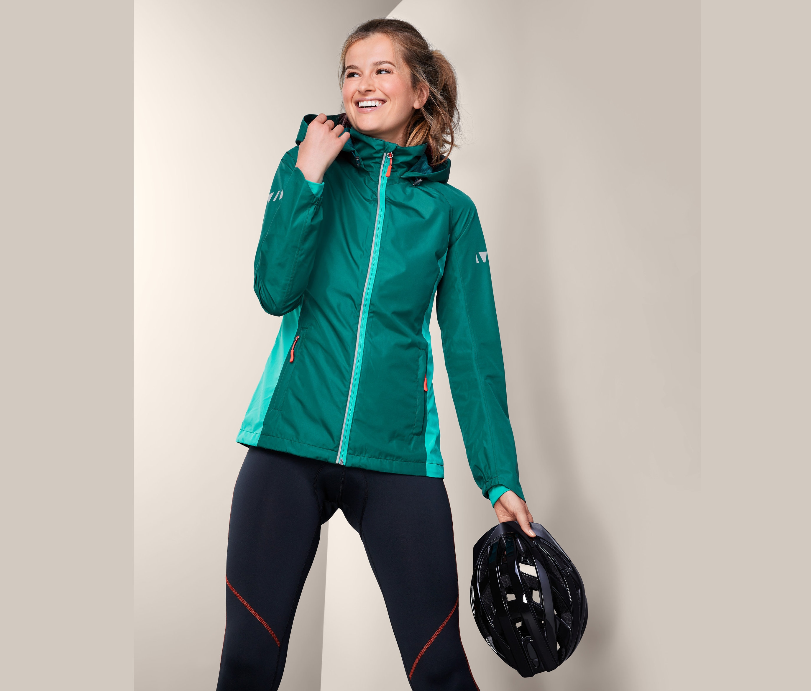 Lächelnde Frau posiert in Velo-Regenjacke und hält einen Fahrradhelm.