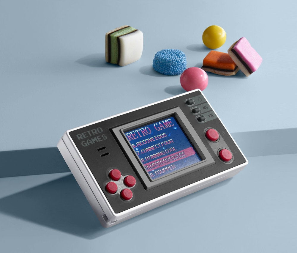 Eine Retro-Mini-Spielekonsole liegt auf einer blauen Oberfläche neben Süßigkeiten.