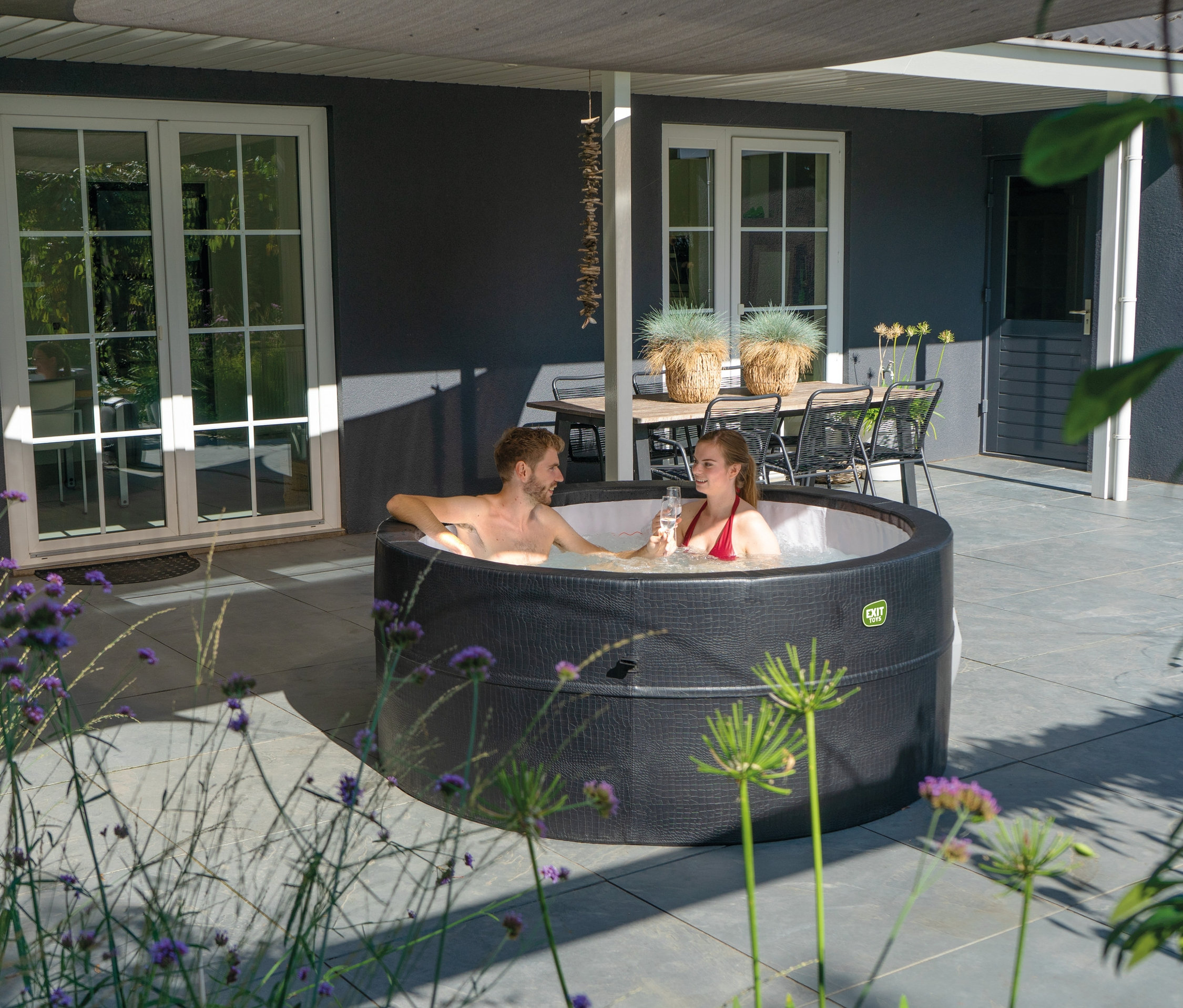 Ein Mann und eine Frau sitzen in einem EXIT Leather Premium Whirlpool für 4 Personen und trinken ein Glas.