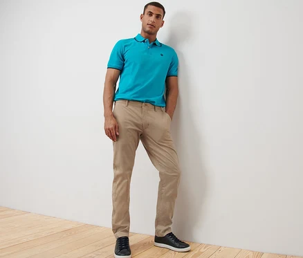 Mann posiert in beigen Chinos und blauem Poloshirt.