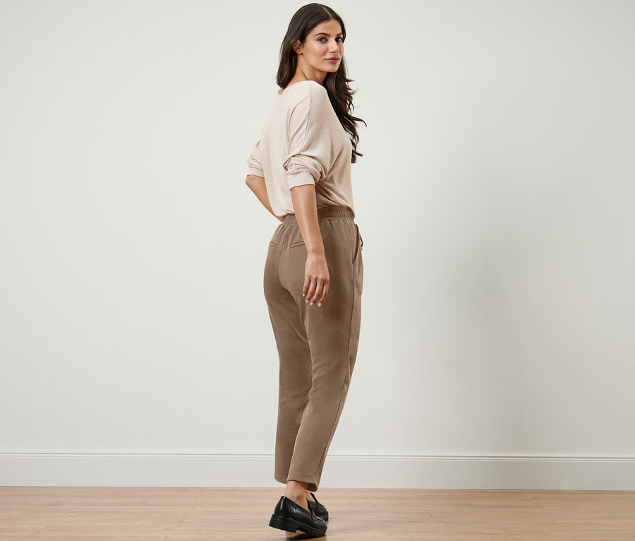 Frau blickt über die Schulter und trägt eine beige Joggpants.