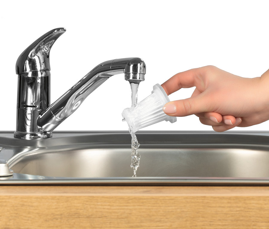 Eine Hand hält einen Filter unter fließendes Wasser aus einem Wasserhahn in einem Edelstahlspülbecken. Es könnte sich um einen Akku-Handstaubsauger Filter handeln.