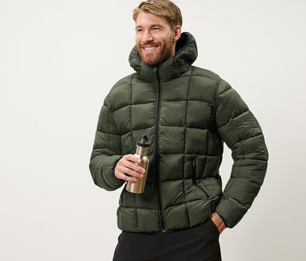 Mann hält eine Wasserflasche und trägt eine khaki Steppjacke.