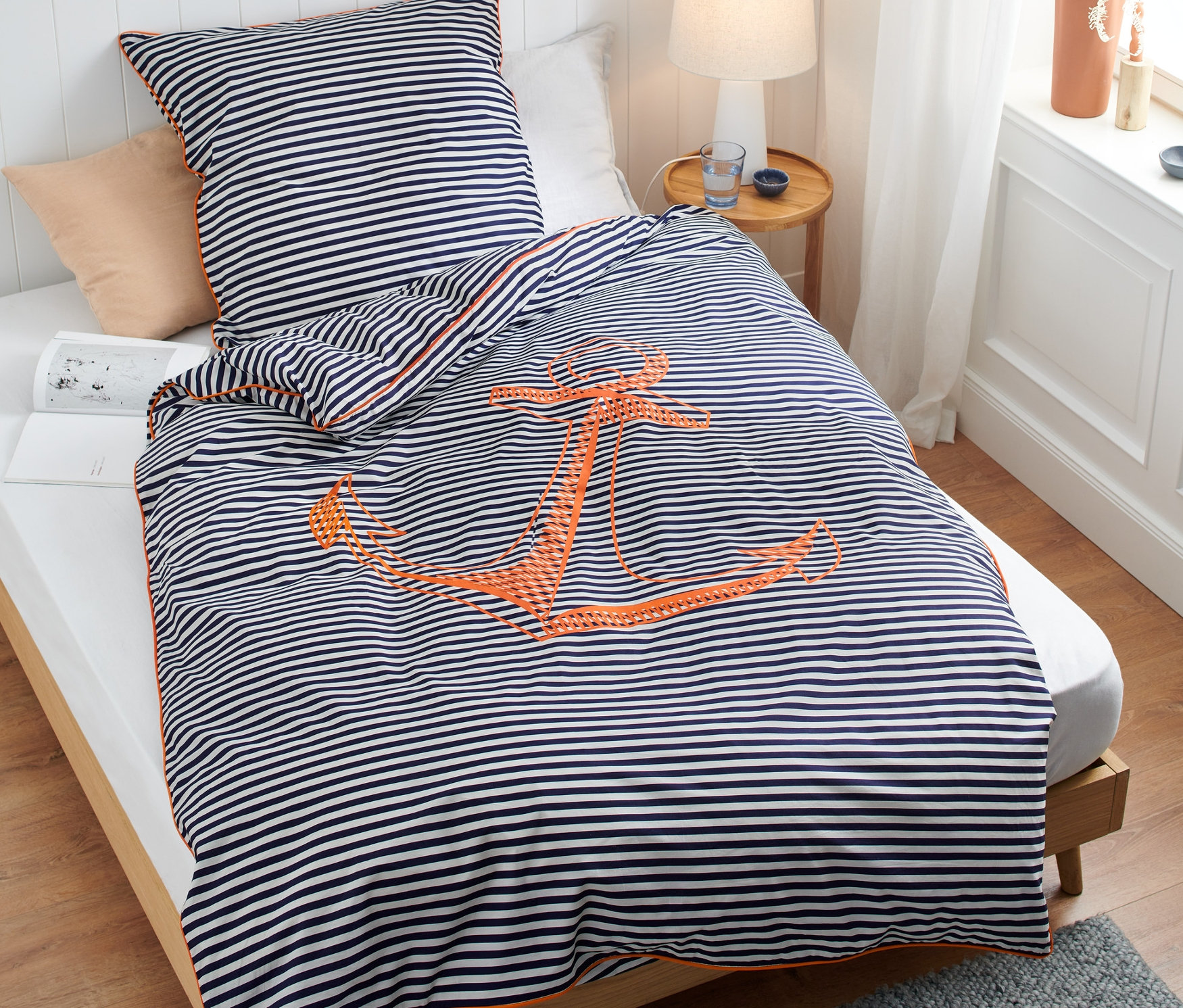 Ein Bett mit orangefarbener Perkal-Bettwäsche in Standard- und Übergröße mit einem Ankermotiv.