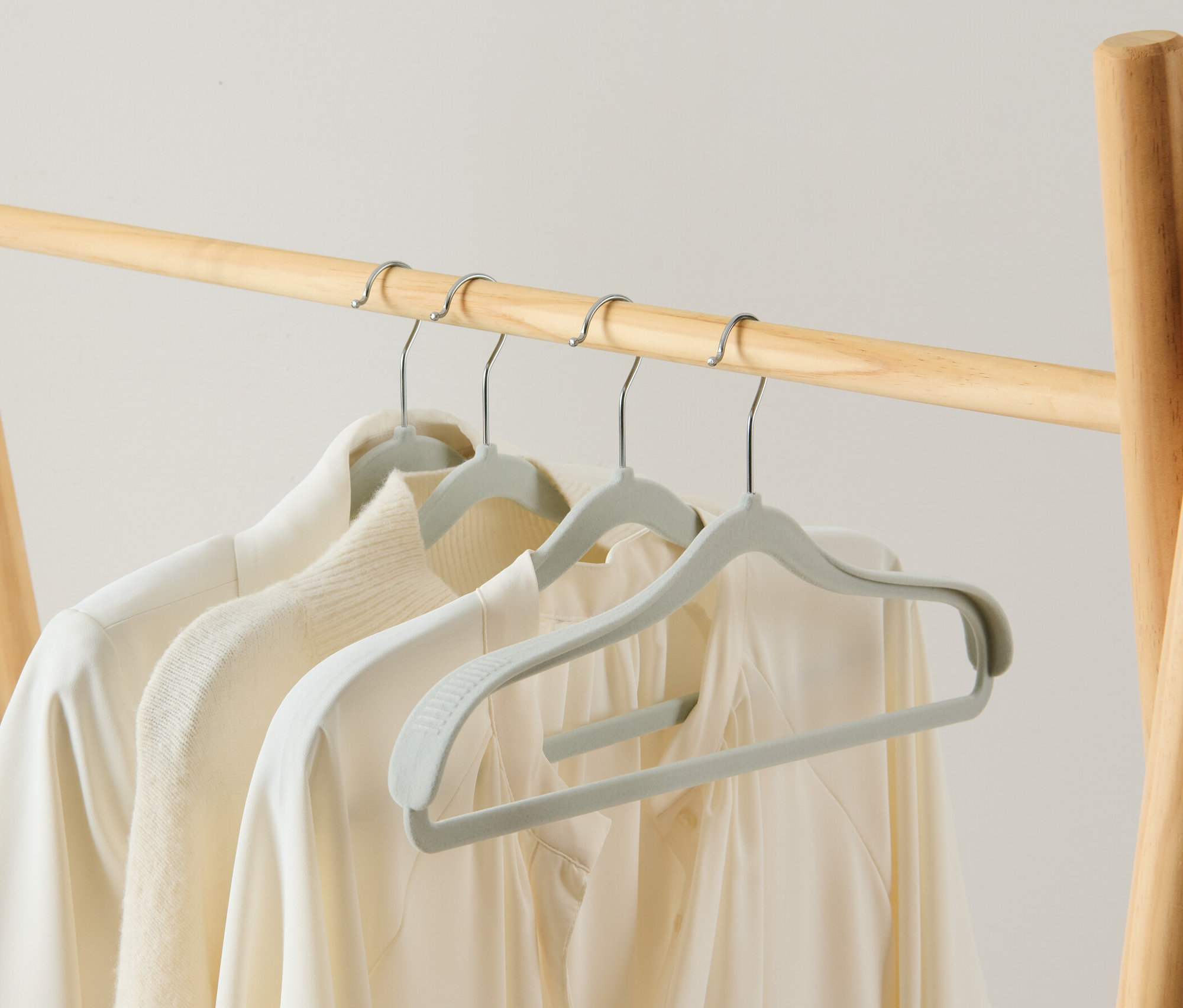 An einer Holzgarderobe hängen drei 4 schulterverstärkte Kleiderbügel mit weißer Kleidung.