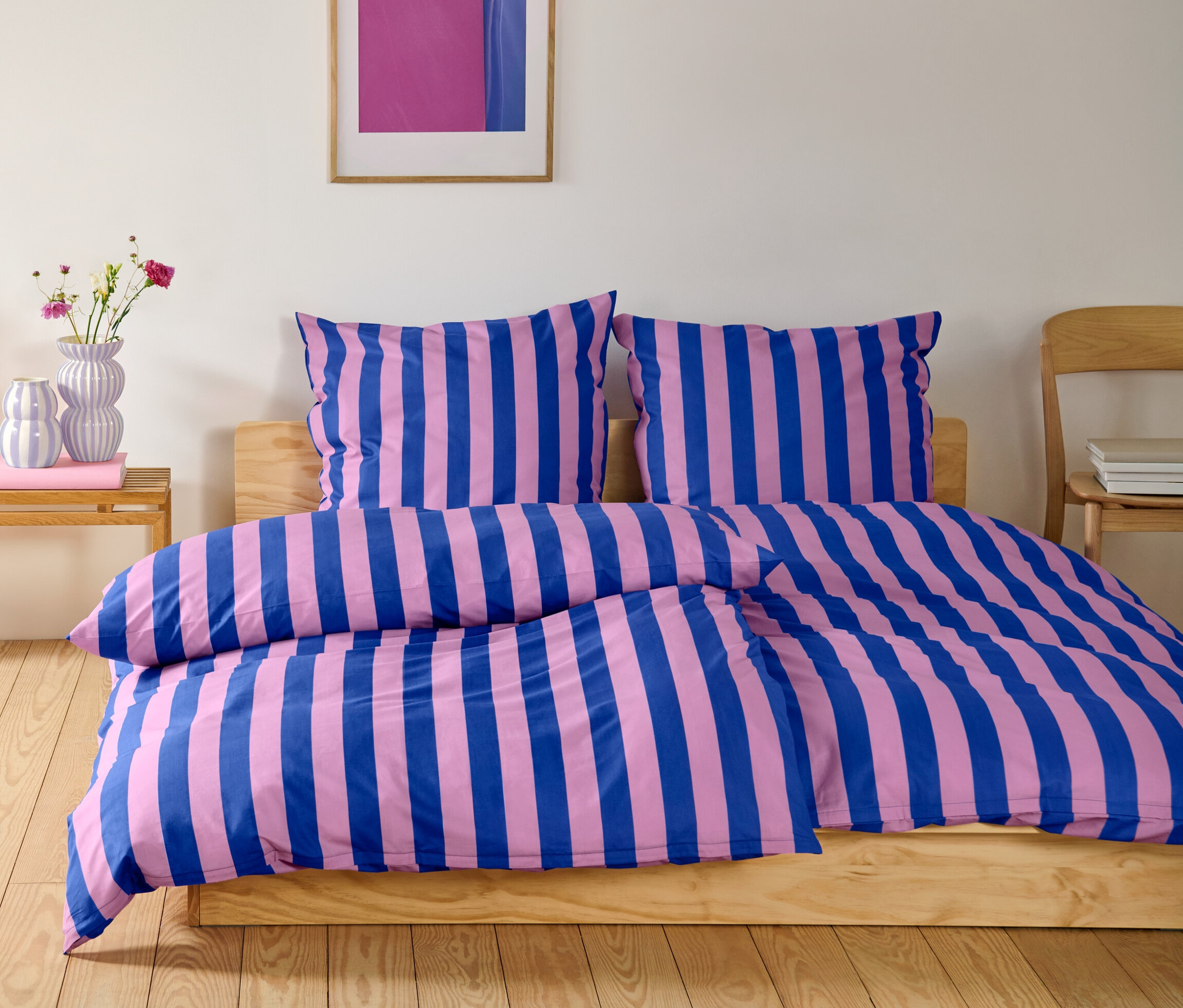 Schlafzimmer mit einem Bett mit normalgroßer Perkal-Bettwäsche und übergroßer Perkal-Bettwäsche mit blauen und rosafarbenen Streifen.