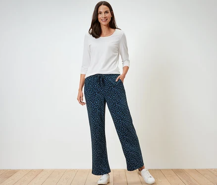 Eine Frau steht und trägt ein weißes Langarmshirt und eine bedruckte Sweathose.