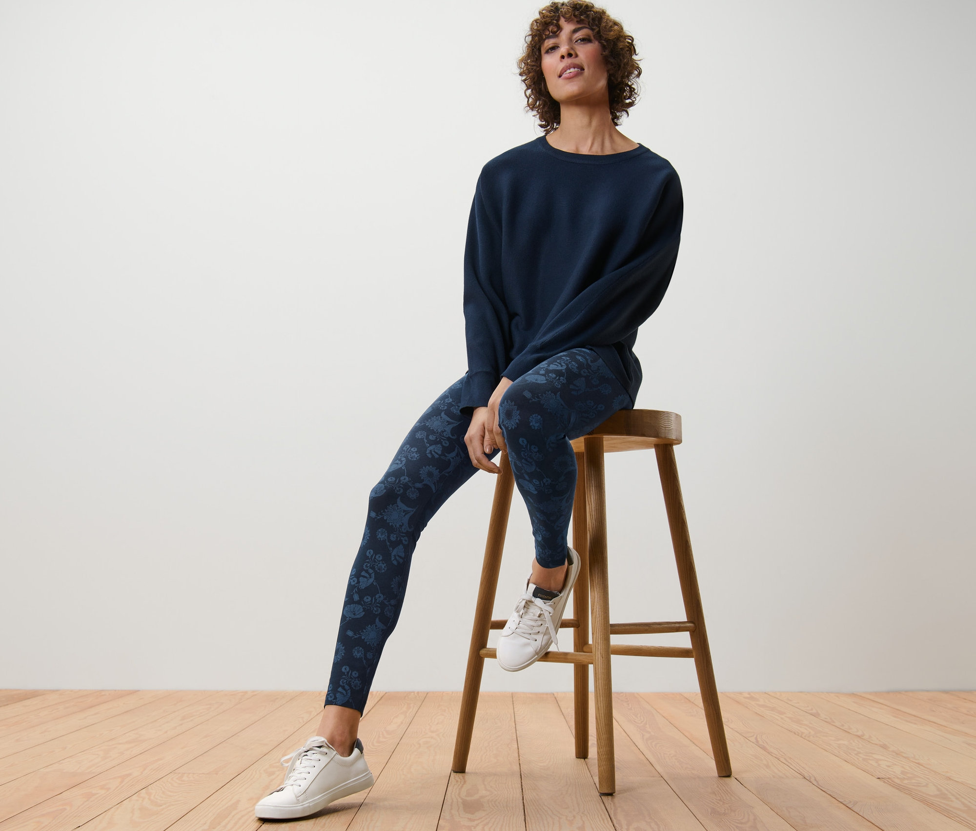 Frau sitzt auf einem Holzhocker und trägt eine bedruckte Leggings.