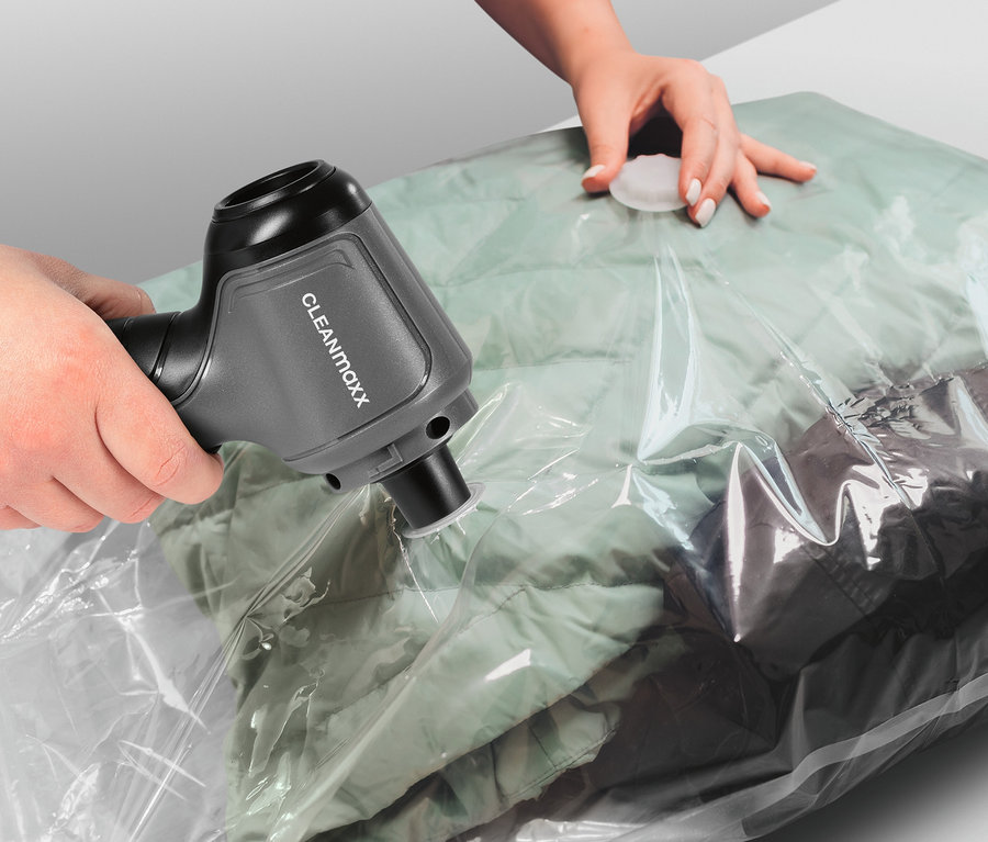 Frau benutzt Akku-Handstaubsauger, um einen Beutel mit Kleidung zu vakuumieren.