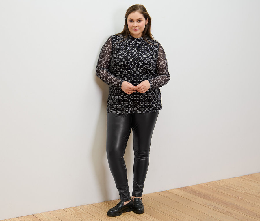 Frau posiert in Leggings in Lederoptik und bedrucktem Mesh-Rollkragenshirt.