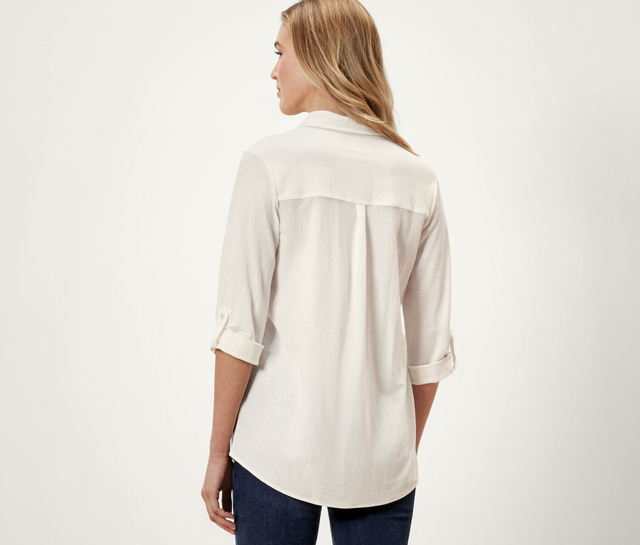 Rückansicht einer Frau in einer cremeweißen Piqué-Jerseybluse und blauen Jeans.