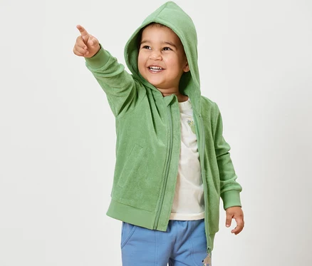 Junge zeigt in grüner Kinder-Frottier-Jacke mit dem Finger.