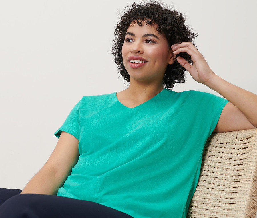 Frau sitzt auf einem Stuhl und trägt ein Shirt aus Leinenmix in Aqua.