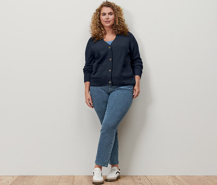 Eine Frau lehnt an einer Wand und trägt eine dunkelblaue Strickjacke mit Wolle und eine Strickjacke.