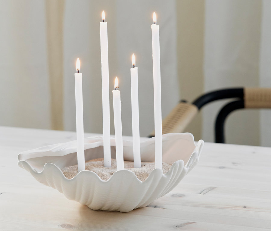 Fünf weiße Kerzen brennen in einer weißen Schale »Shell« mit Sand auf einem Tisch.