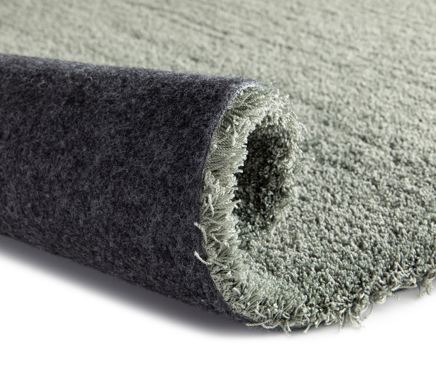Detailansicht des Teppichs »Mellow«, grün, ca. 60 x 115 cm, der teilweise aufgerollt ist und eine dunkelgraue Unterseite zeigt.