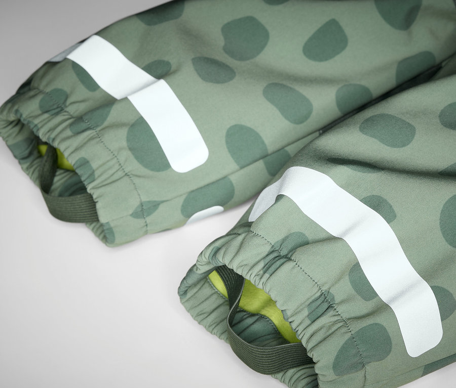 Detailansicht eines Kinder-Softshell-Einteilers mit olivgrünem Muster und weißem Reflexstreifen.