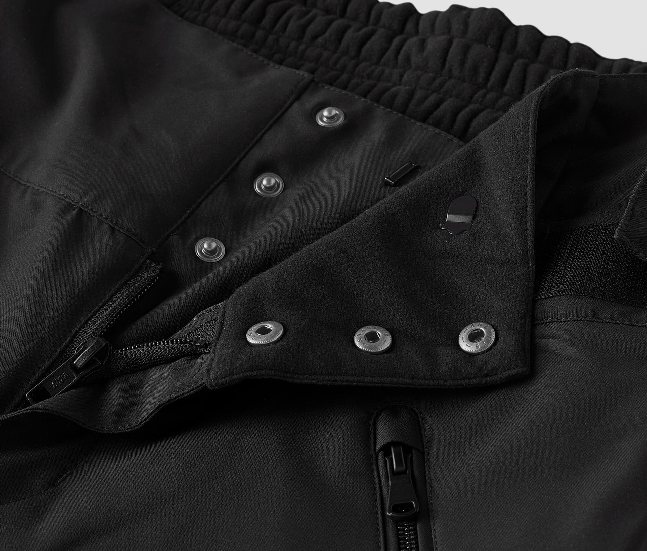 Detailaufnahme eines schwarzen Stoffes mit Knöpfen und Reißverschluss.