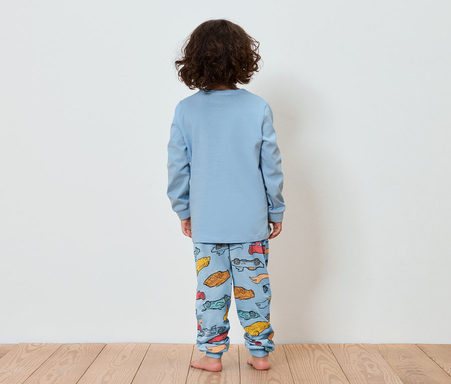 Ein Kind mit dem Rücken zur Kamera trägt einen blauen Pyjama mit einem Aufdruck von kleinen Autos.