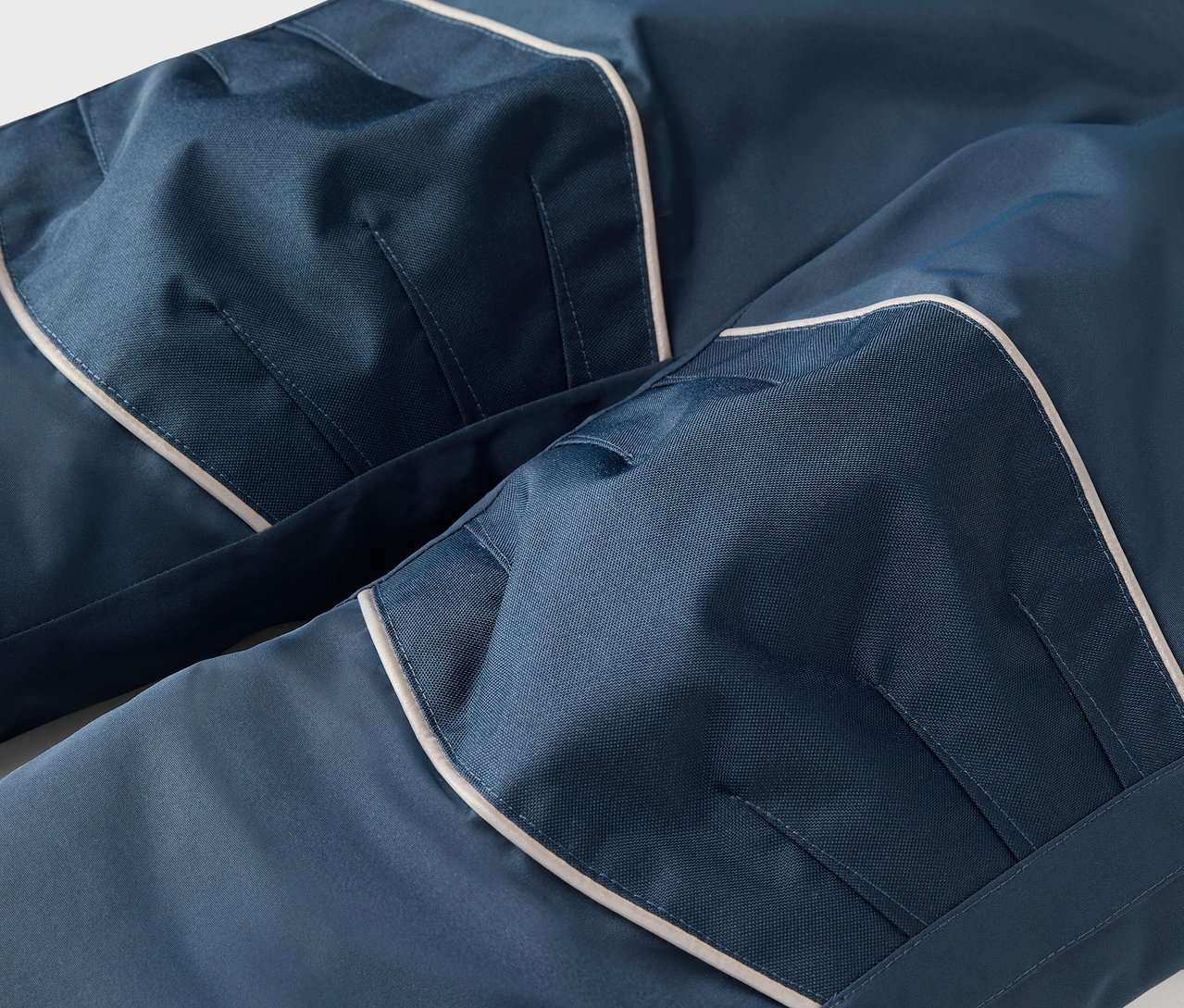 Detail einer blauen Hose mit weißer Paspelierung und Taschen.