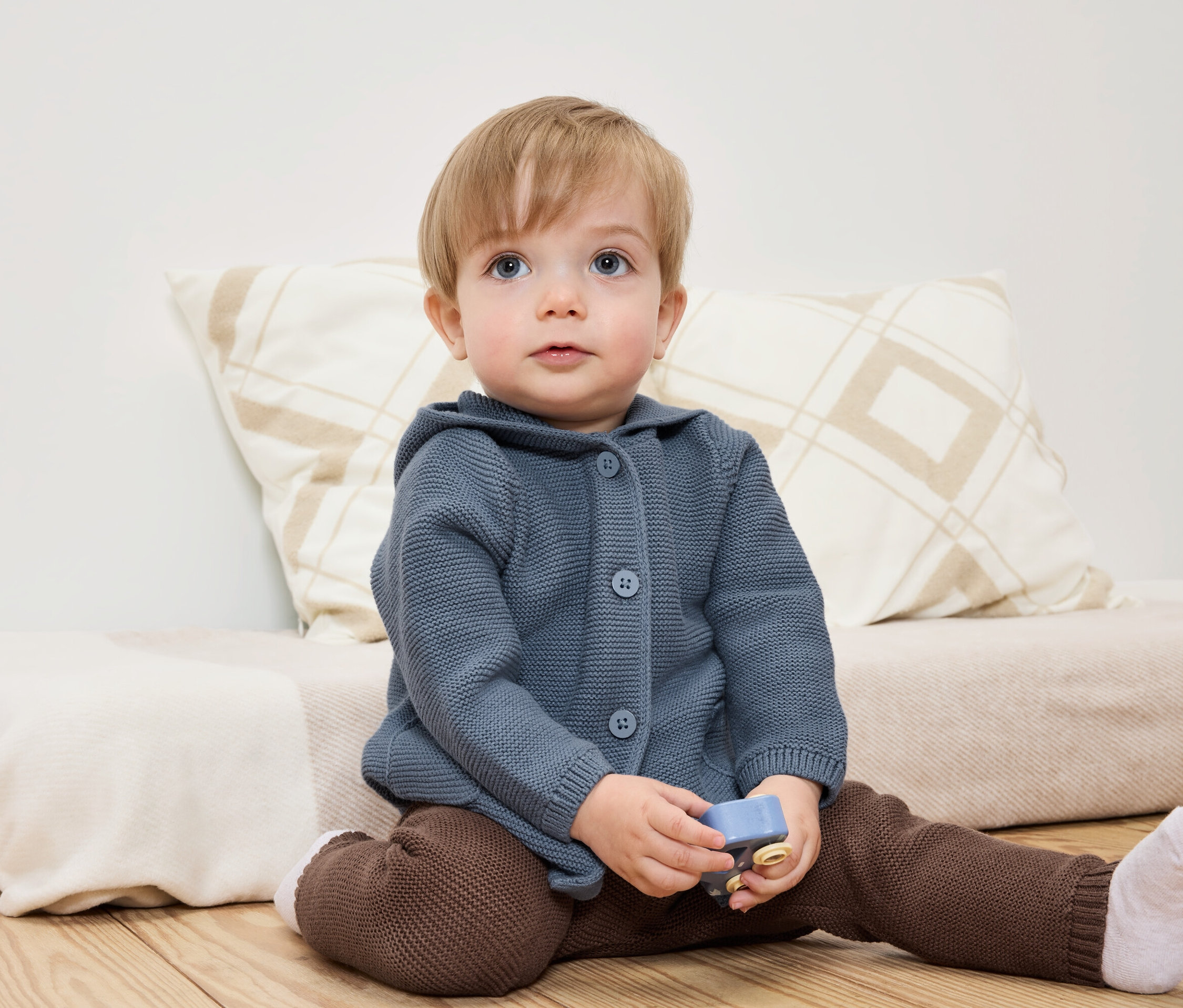 Ein Kind sitzt mit einem Spielzeug in der Hand auf dem Boden.