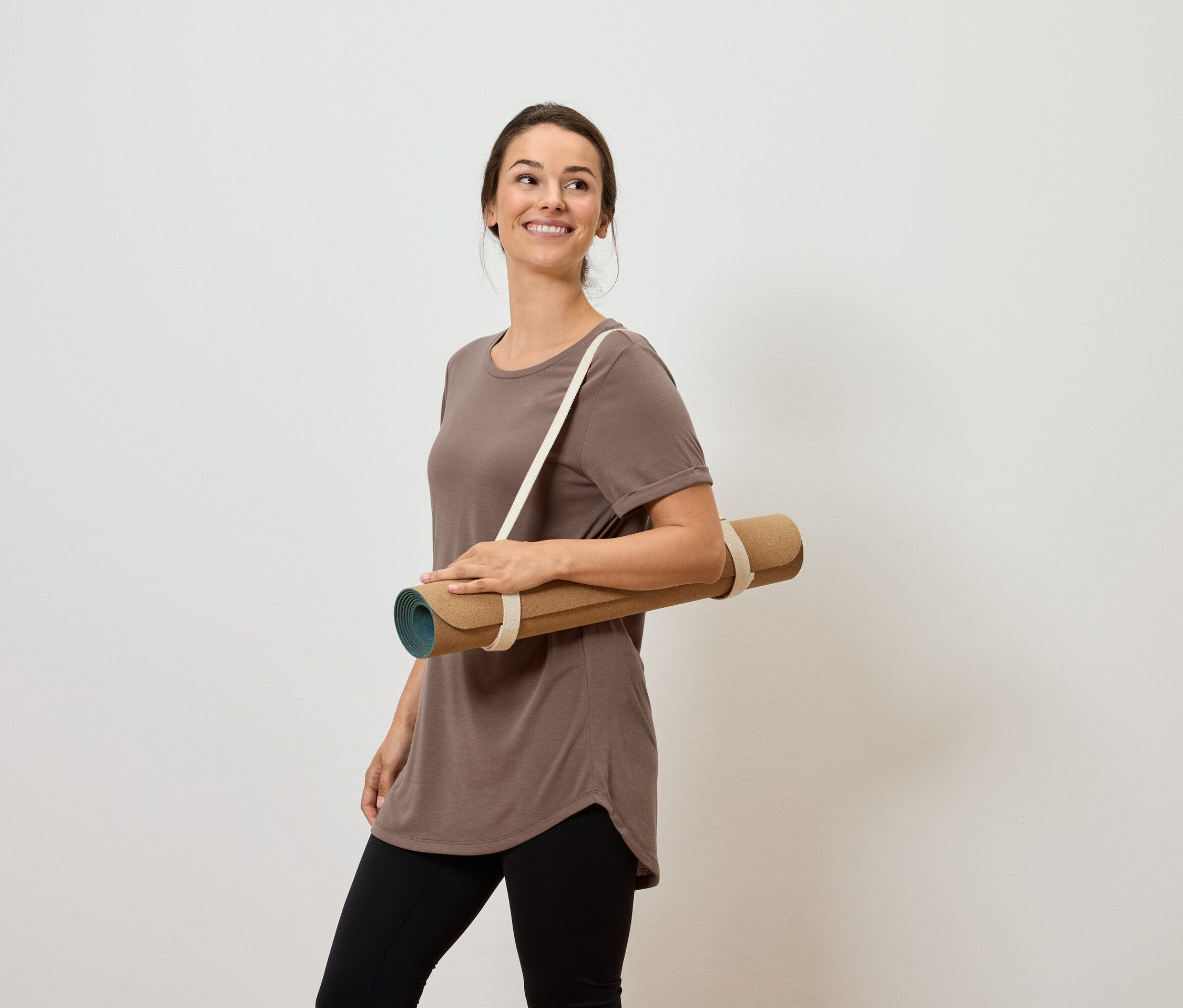 Lächelnde Frau trägt Yogamatte über der Schulter.