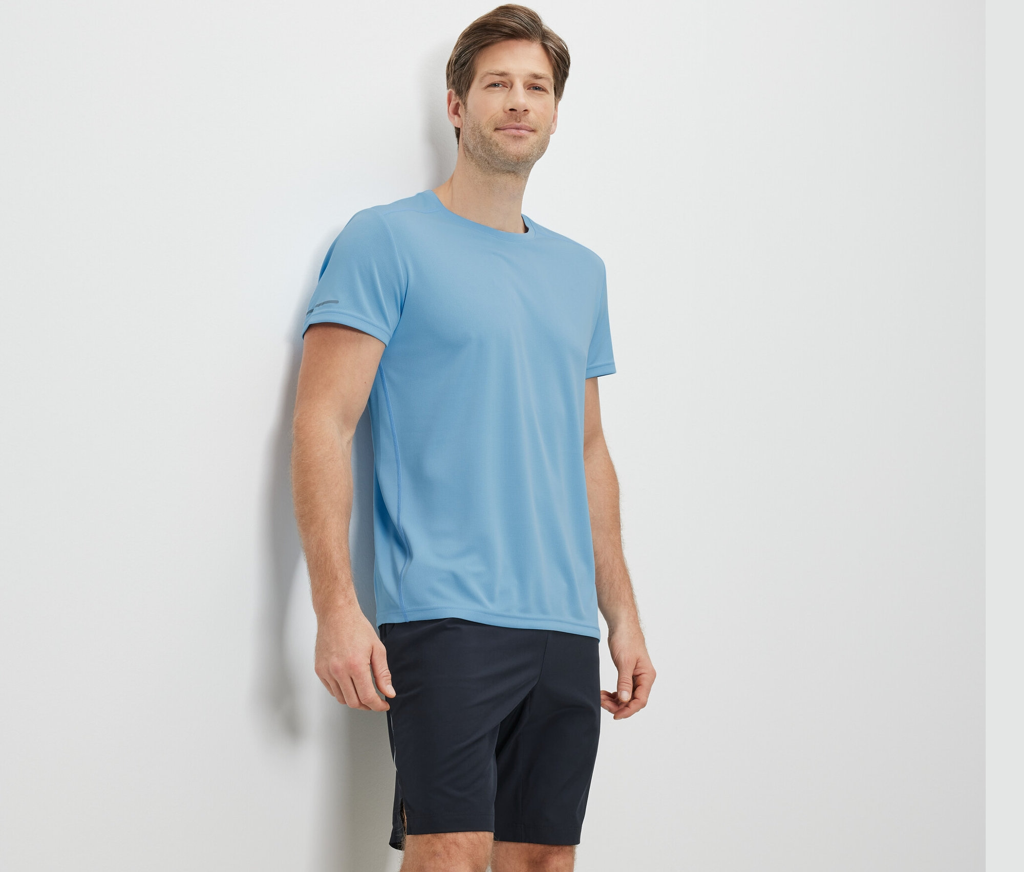 Mann lehnt an Wand, trägt hellblaues Funktionsshirt.