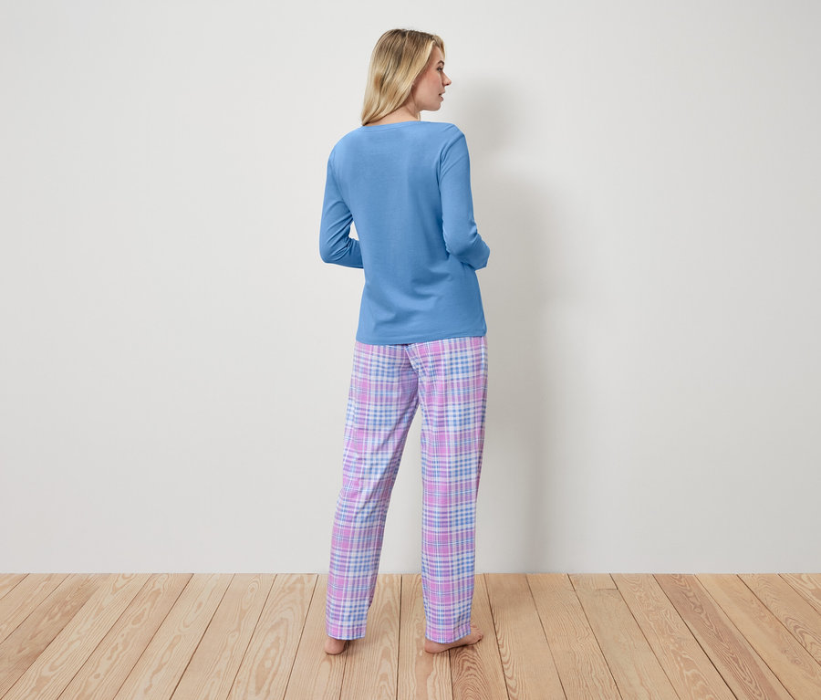 Frau im blauen Pyjama-Oberteil und karierter Hose steht mit dem Rücken zur Kamera.