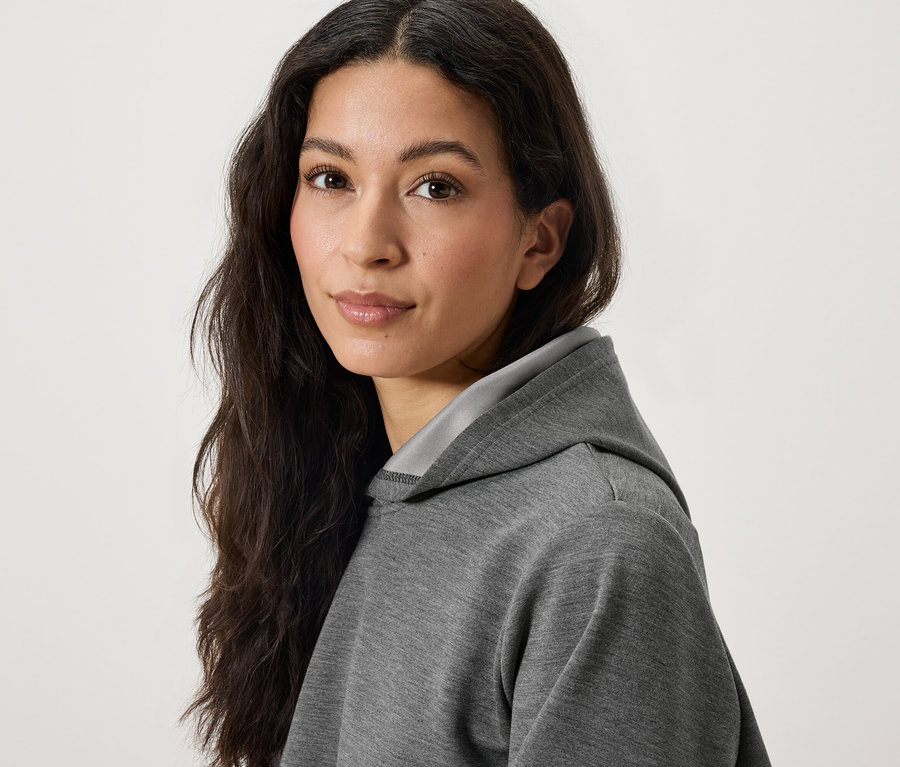 Porträt einer Frau mit langen, dunklen Haaren in einem grauen Kapuzenpullover.