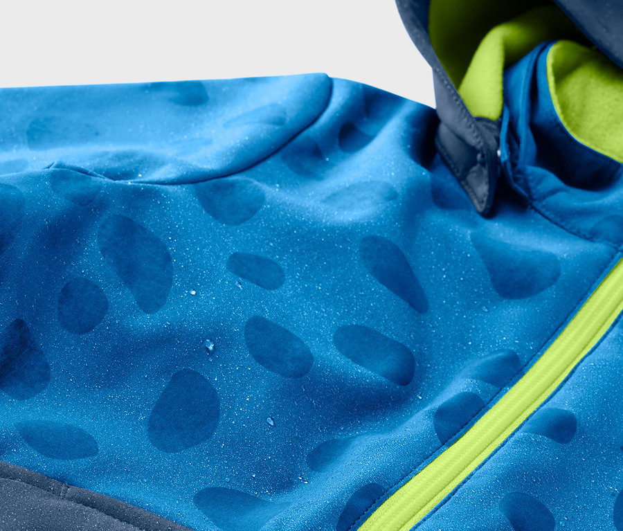 Detailansicht einer blauen Kinder-Softshelljacke mit Farbwechsel bei Regen und grünem Reißverschluss.
