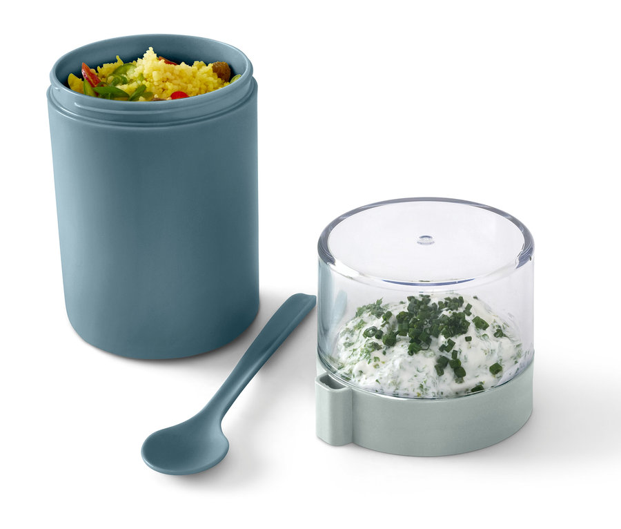 Ein grüner To-go-Joghurt-Becher mit Inhalt, daneben ein Löffel und ein Behälter mit Kräuterquark.