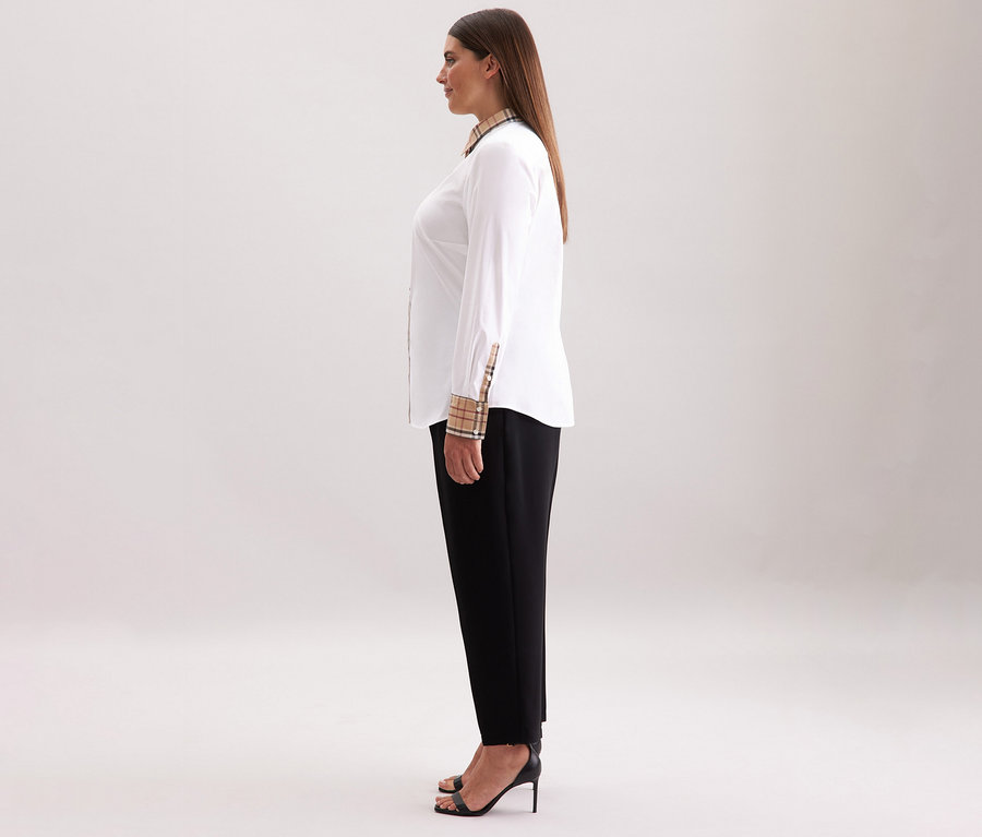 Frau steht seitlich und trägt eine weiße Seidensticker Popeline-Bluse mit Karodetail, schwarze Hose und schwarze High Heels.