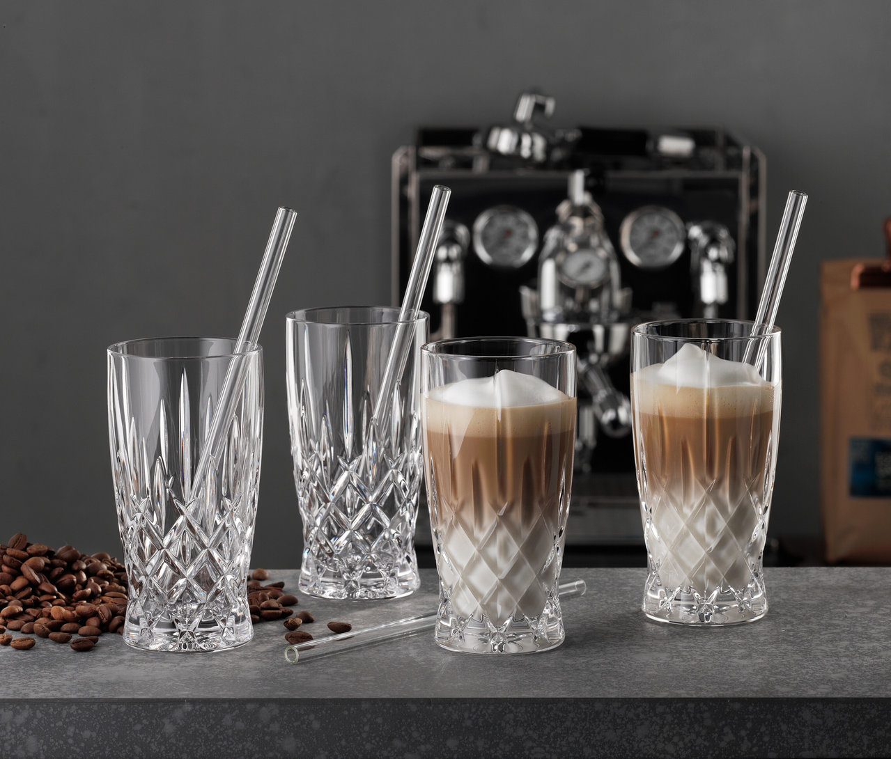Vier Nachtmann Latte Macchiato Gläser »Noblesse« mit Glastrinkhalmen stehen auf einer Theke, zwei davon gefüllt mit Latte Macchiato.