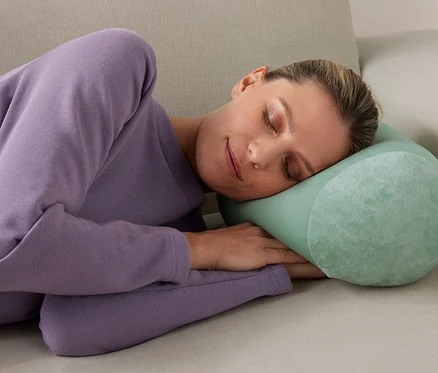 Frau schläft mit Relaxkissen auf Sofa.