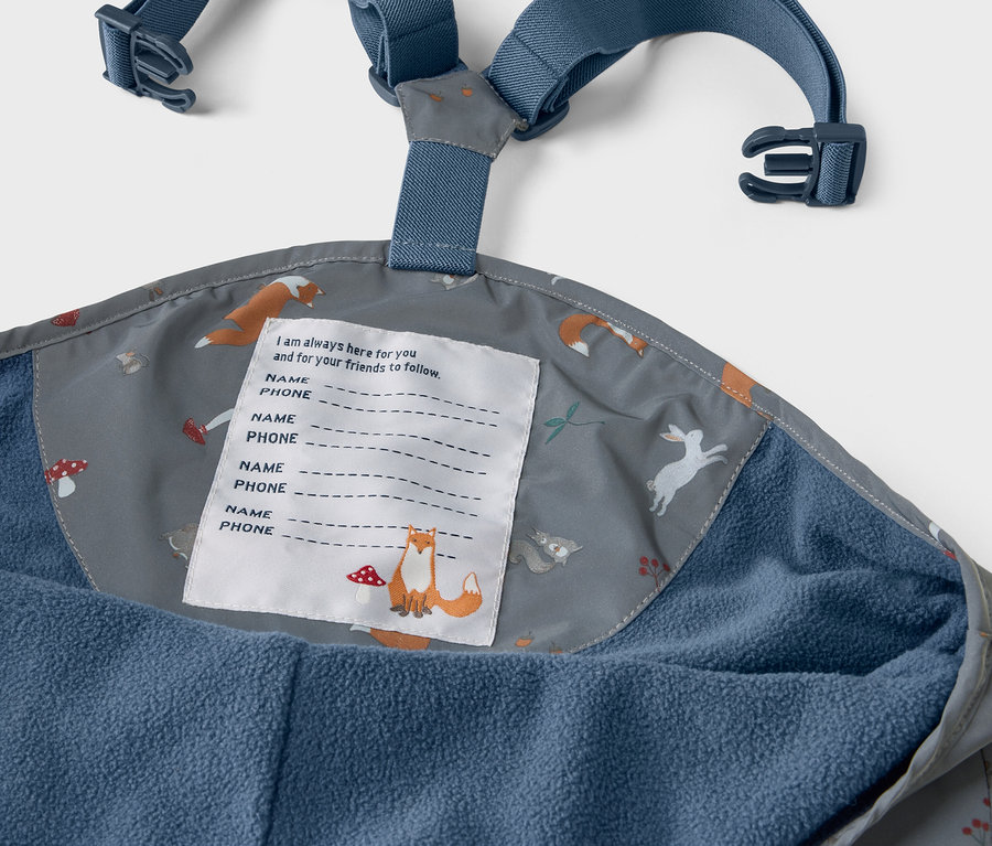 Detail einer Kinder-Thermo-Regenhose mit reflektierenden Designelementen, Innenseite der Hose mit Aufdruck von Füchsen, Hasen und Pilzen.