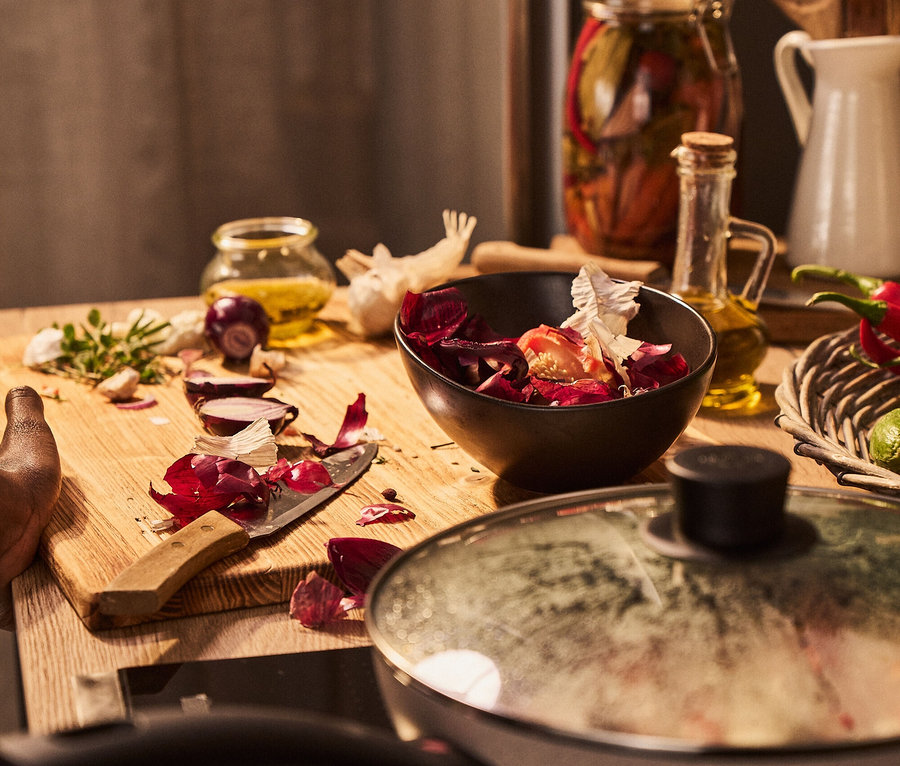 Holzbrett mit geschnittener Zwiebel, Messer, Knoblauch und einer Schüssel Gemüse neben einem Topf auf dem Herd.