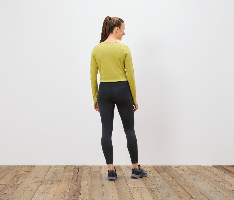 Frau mit dem Rücken zur Kamera trägt ein olivgrünes Langarmshirt, schwarze Leggings und Turnschuhe.